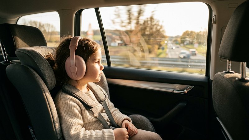 Un niño pequeño con unos auriculares protectores de color suave puestos, sentado tranquilo en el asiento trasero de un c