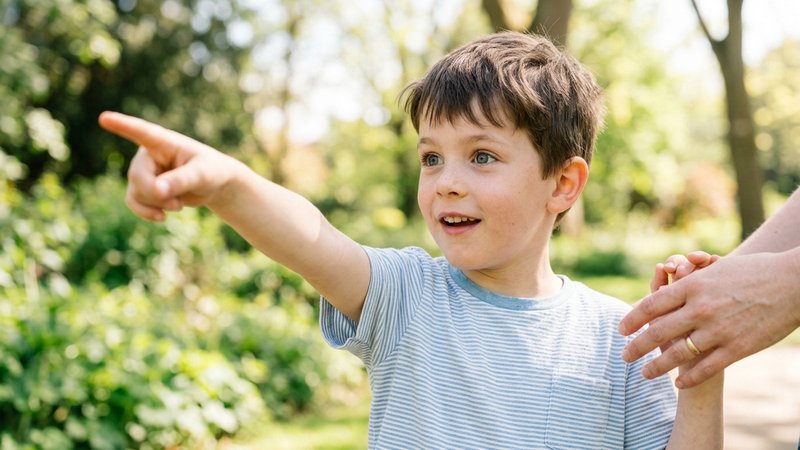 Un primer plano medio de un niño pequeño señalando con el dedo índice hacia algo fuera de plano, con la mirada muy despi